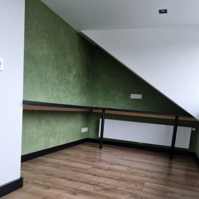 Moderne zolderkamer met groene wandafwerking, houten vloer en ingebouwde werktafel.