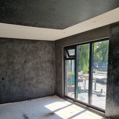 Industrieel interieur met donkere betonstuc wanden, zwart plafond en grote ramen.